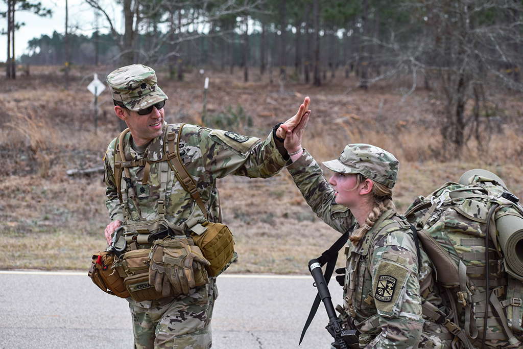 A man and woman dressed in U.S. military uniforms high five each other.