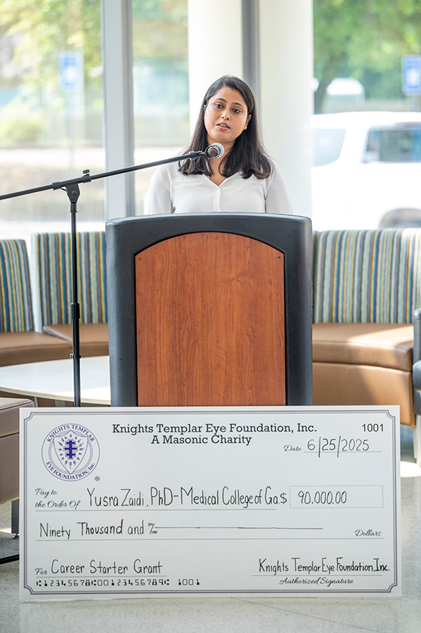 A woman stands at a podium and speaks to a large group of people.