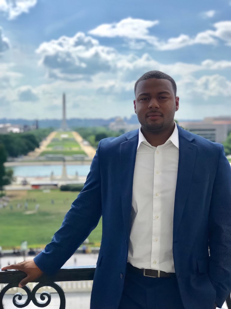Man standing on a balcony with the backdrop of Washington, D.C., pictured behind him.