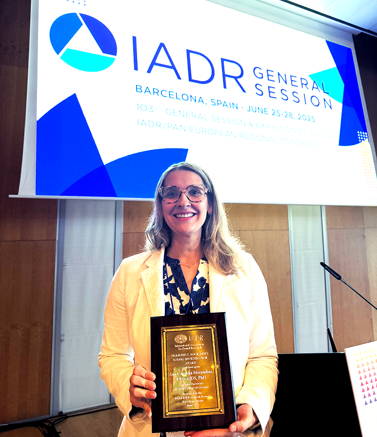 A female periodontist stands on a stage and holds an award plaque.