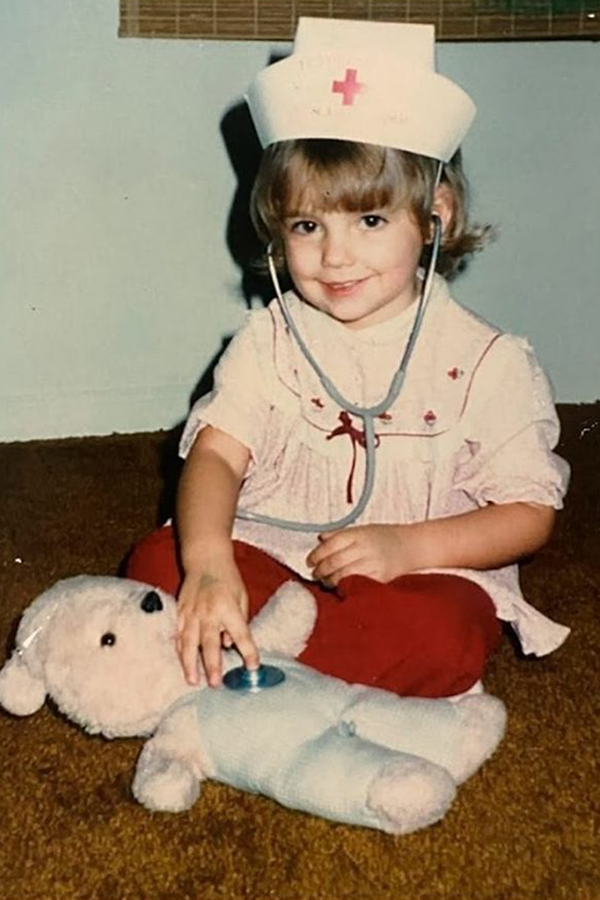 A young child dressed up as a nurse. She is using a stethoscope to "examine" a stuffed animal.
