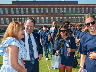 A man and his wife meet with four freshmen college students. They are all standing outside during an event.