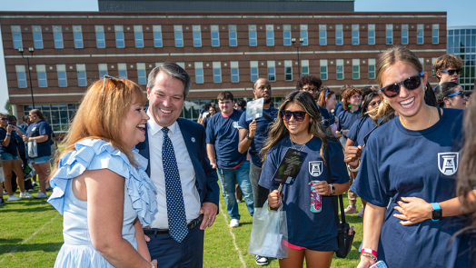 A man and his wife meet with four freshmen college students. They are all standing outside during an event.