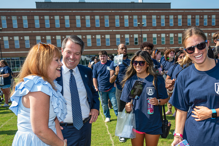 A man and his wife meet with four freshmen college students. They are all standing outside during an event.
