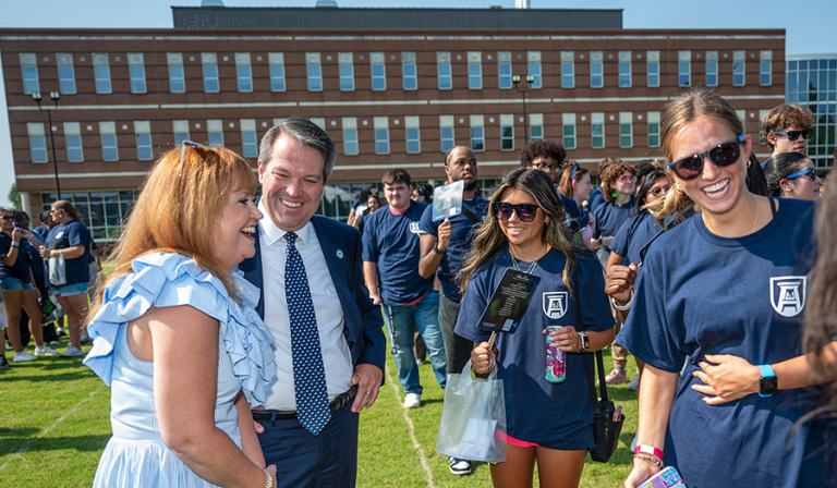 A man and his wife meet with four freshmen college students. They are all standing outside during an event.