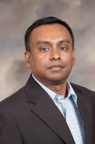 A man in a suit stands in front of a textured background.
