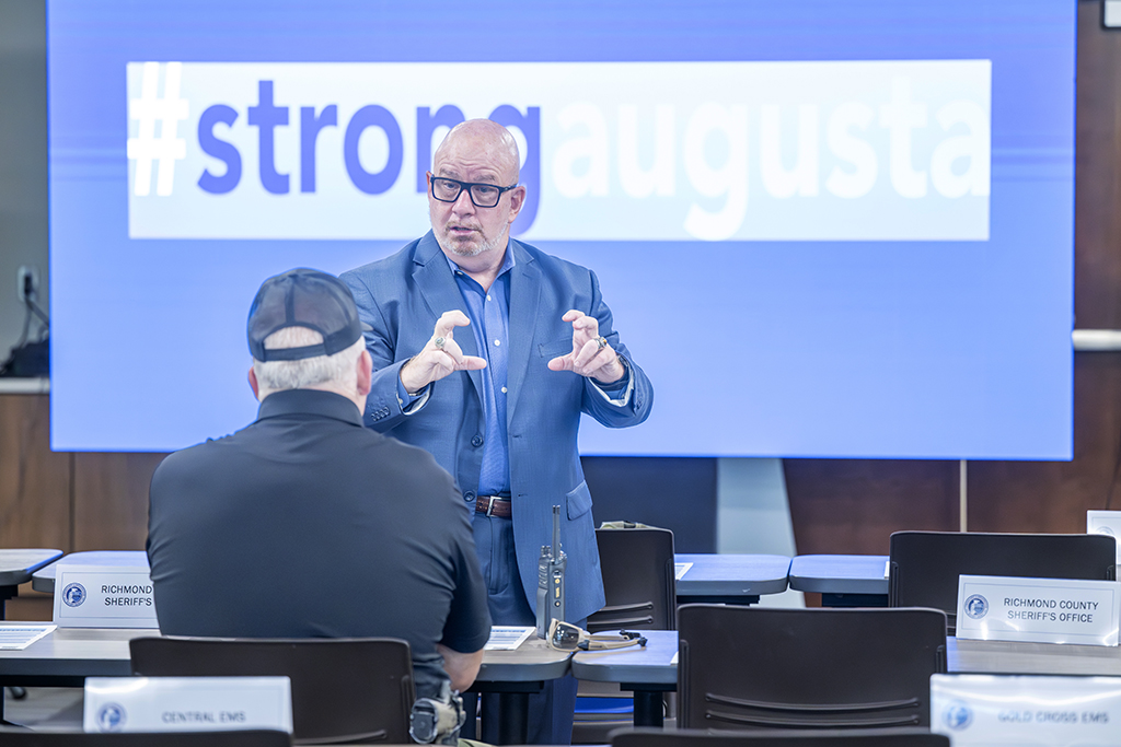 A man stands in front of another man who is seated. They are talking about a presentation.