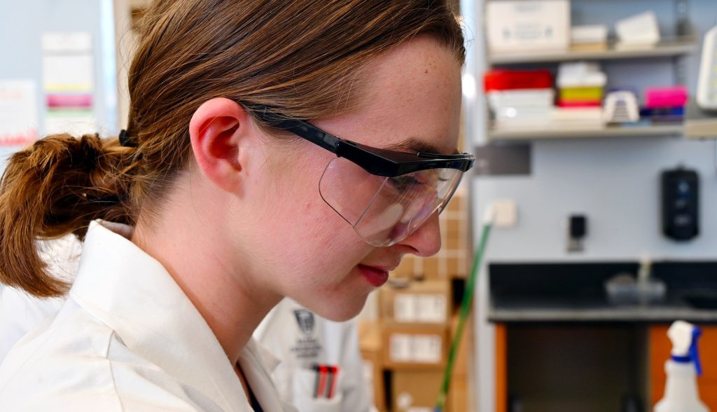 A high school student taking part in a summer scholars program learns about proper lab techniques.