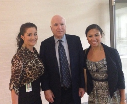 Two women in dresses pose for the camera with a man in a suit stanind between them.