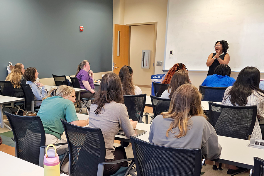 A young, female college professor laughs as she teaches a class full of masters-level students.
