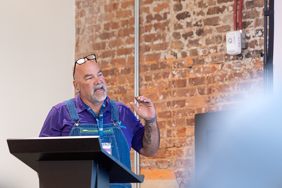 A man stands at a podium and delivers a presentation in front of a large group of people.