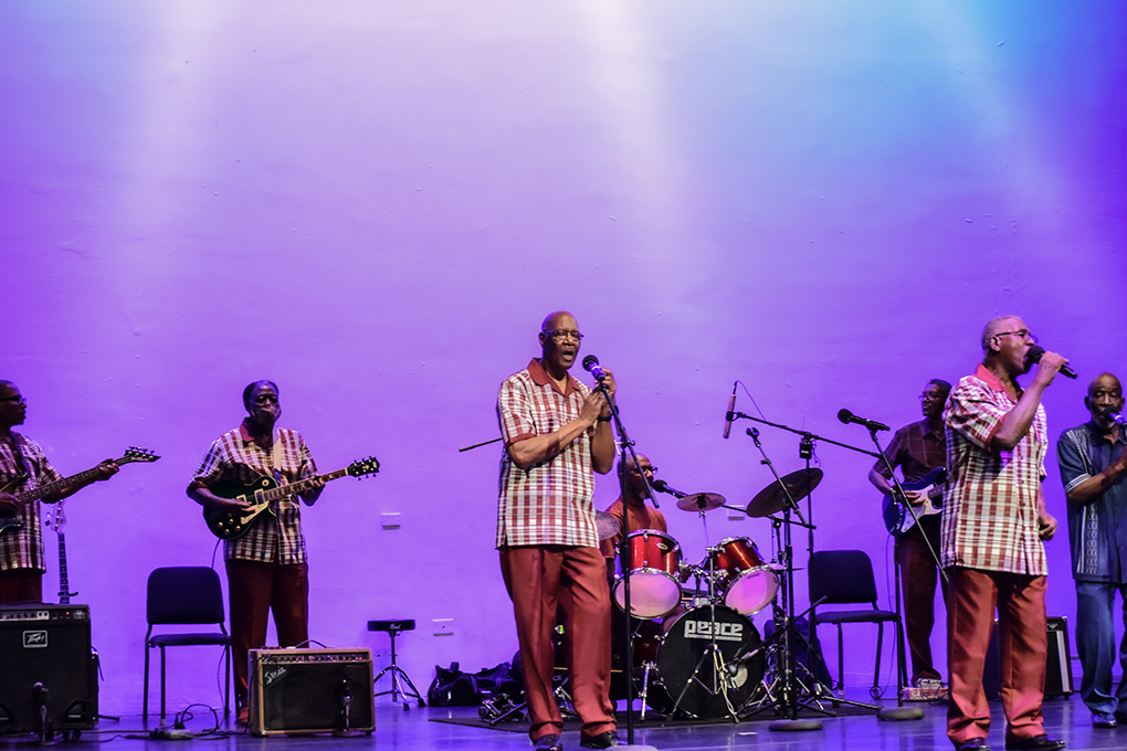 A band of male gospel singers wearing matching outfits perform on stage.