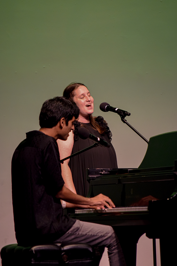 A man plays the piano while a woman sings on stage.