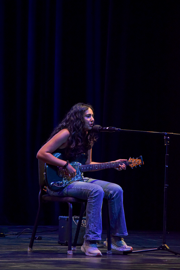 A woman sits down, plays the guitar and sings on stage.