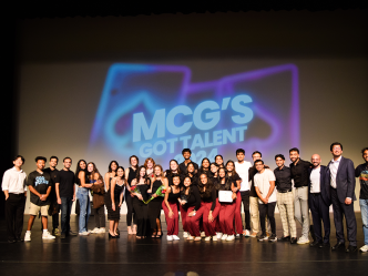 A group of medical students performing in a talent show stand in front of a backdrop that reads "MCG's Got Talent."