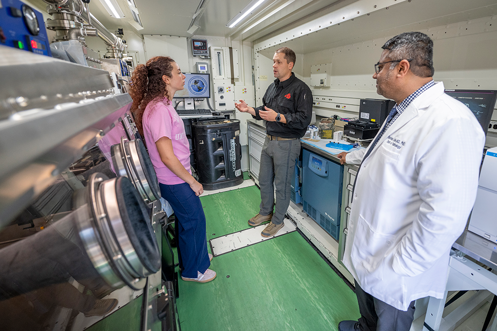 A woman, a male U.S. Air Force captain and a male doctor stand inside a mobil laboratory truck and talk to each other.