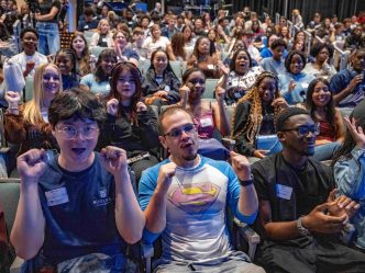 Many college-aged students since inside a building smiling and waving.