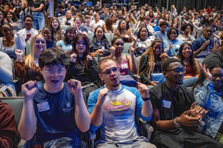 Many college-aged students since inside a building smiling and waving.