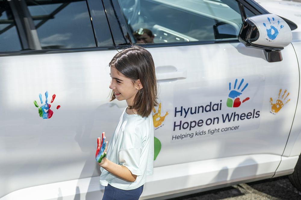 girl smiles at handprint she made on car
