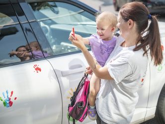 Woman holds child beside car