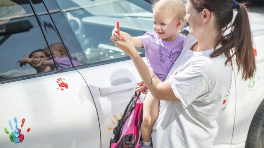 Woman holds child beside car