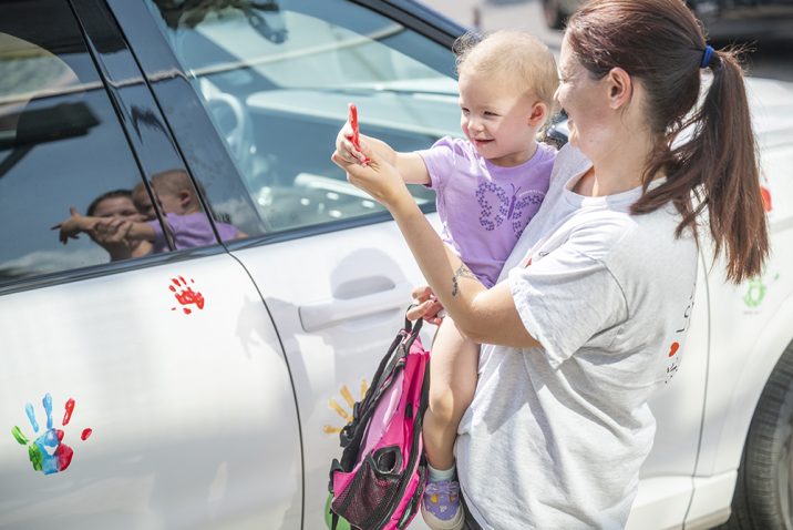 Woman holds child beside car