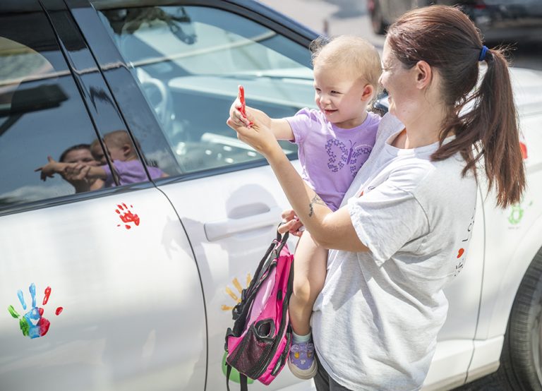 Woman holds child beside car