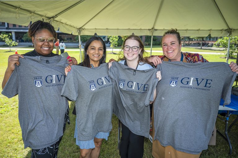 Smiling ladies holding IGIVE t-shirts.