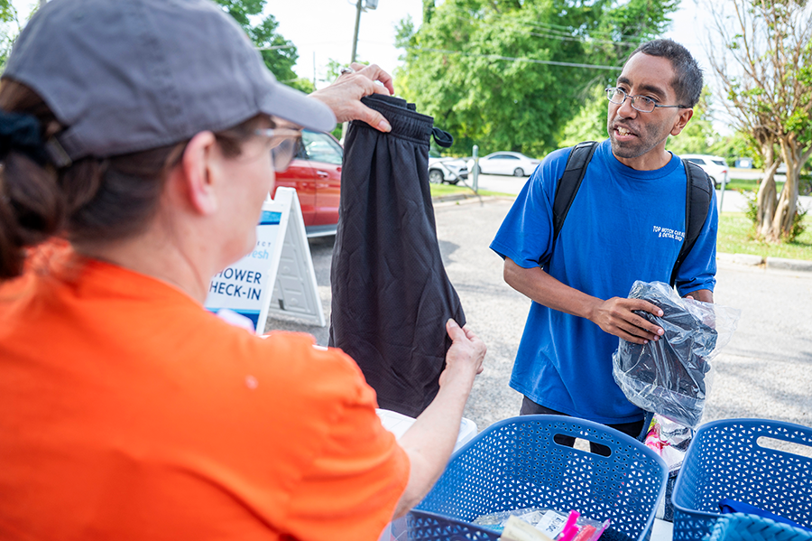 A man speaks with a volunteer at a community event. She hands him fresh clothes for after he takes a shower thanks to a mobile shower unit.