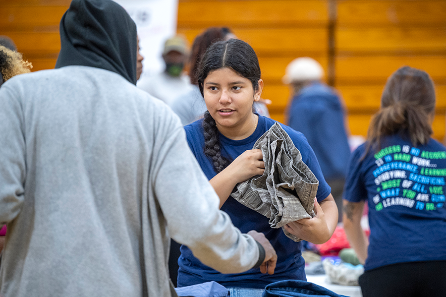 A female college student helps a man find donated clothes that fit him during a community health fair.