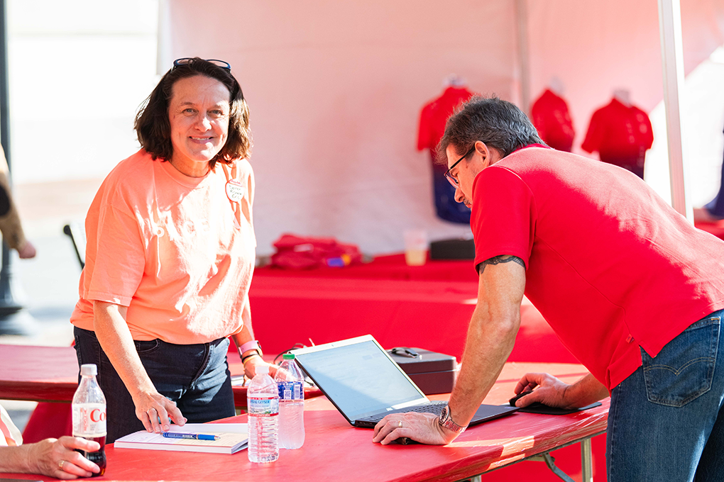 A female volunteer at a fundraising event smiles at the camera while a man looks at a laptop on the other side of a table.