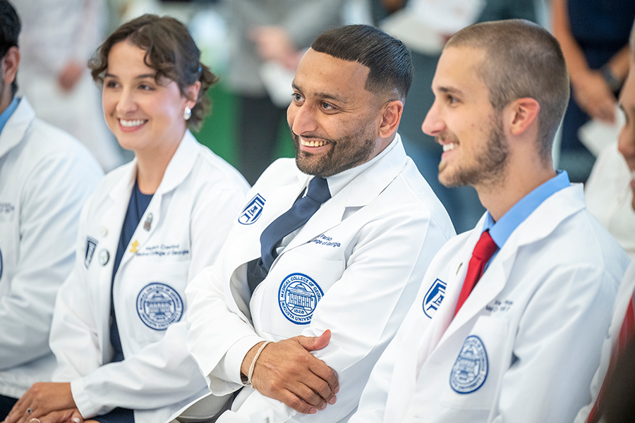 A group of medical students sit on the front row of a large group of people during a ceremony recognizing them for an achievement.