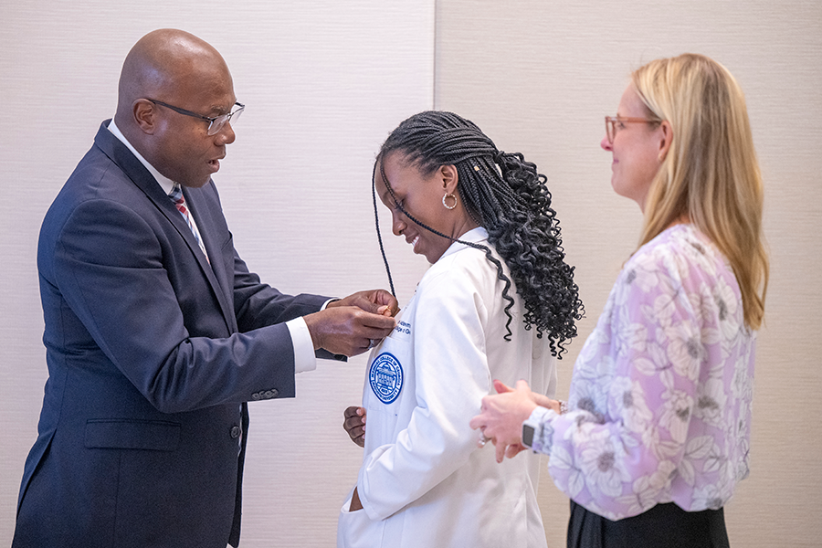A female medical student has a pin placed on her lab coat by a man during a special ceremony.