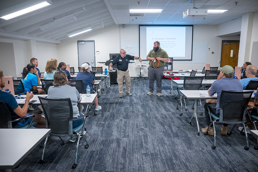 Two men demonstrate how to properly use a Stop the Bleed kit to a room filled with college coaches.