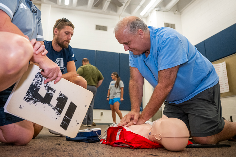 Three college athletics coaches learn how to administer CPR using a dummy.