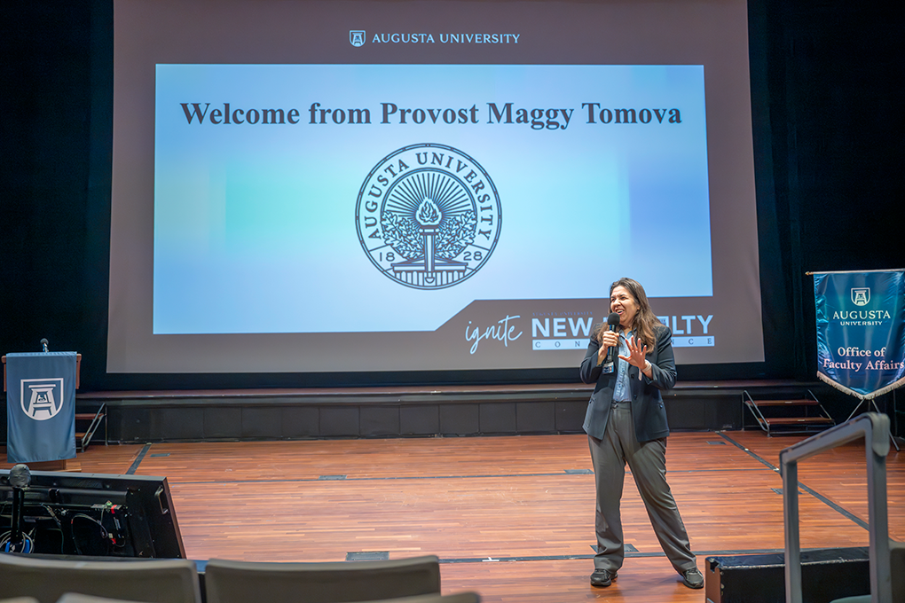 Woman stands in front of a large screen holding microphone.