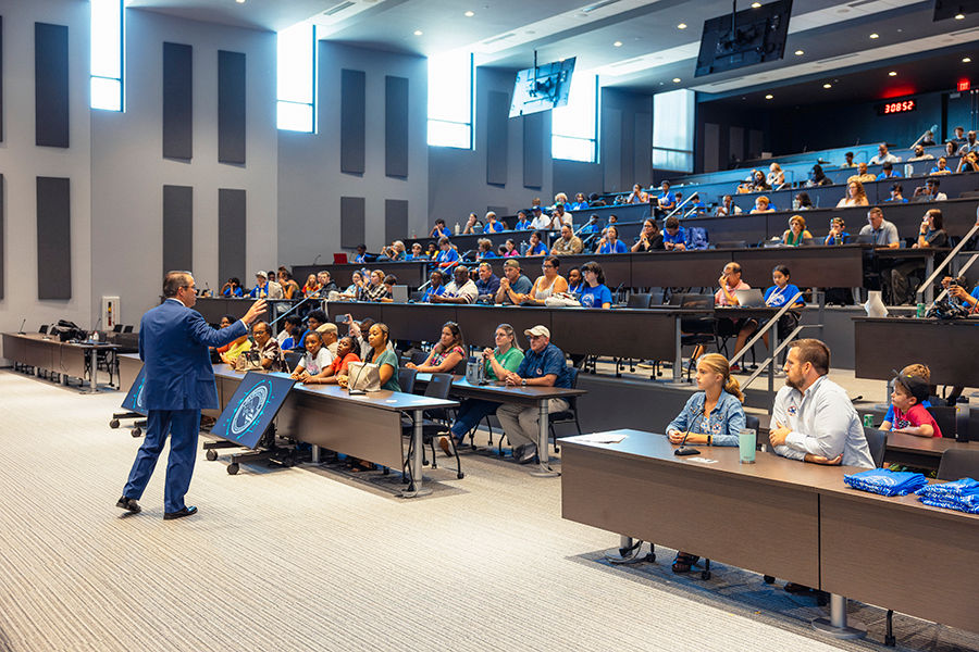 A man speaks to a large crowd in a large auditorium.