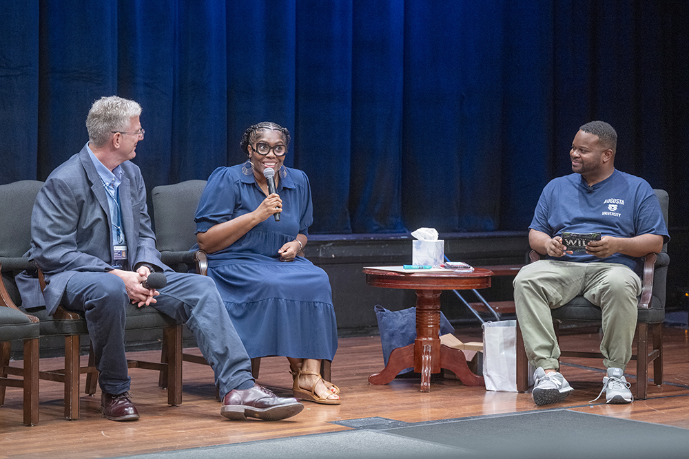 two men and one woman sitting in chairs and talking.
