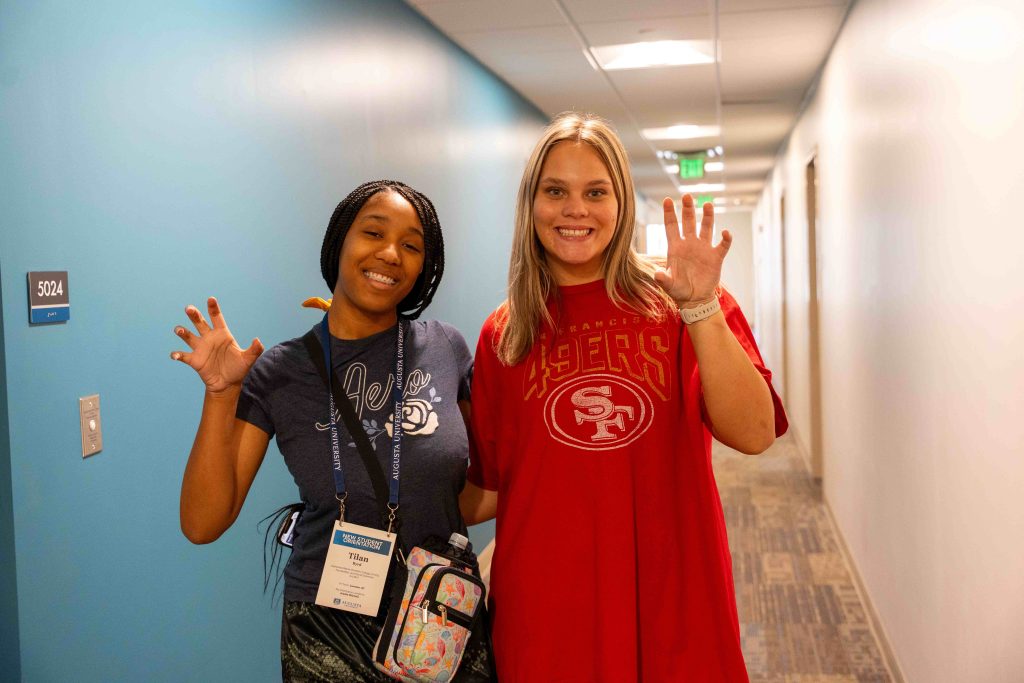 Two college-aged females holding up their hands in a paw formation while inside a building hallway.