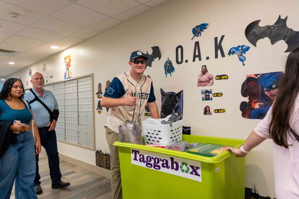 A college-aged man pushes a large box filled with personal belongings.