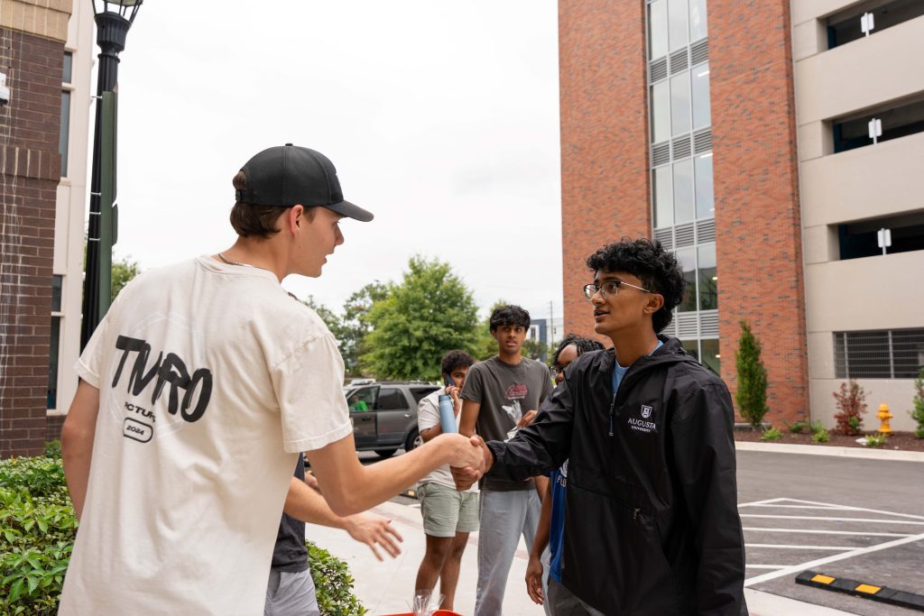 Two college-aged males shake hands.