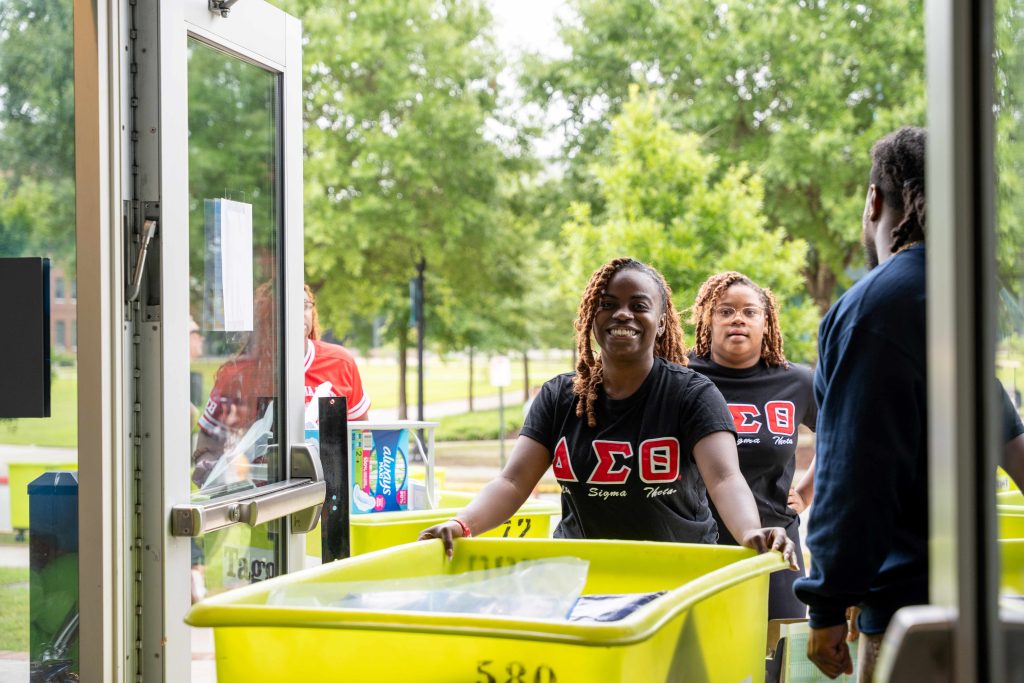 A college-aged female pushes a large box into a building.