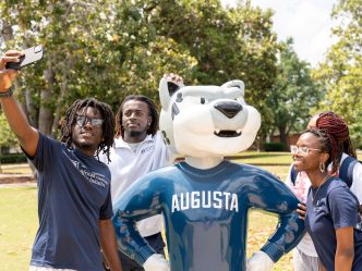 Four students surround the Augusta University mascot, Augustus, while taking a group picture.