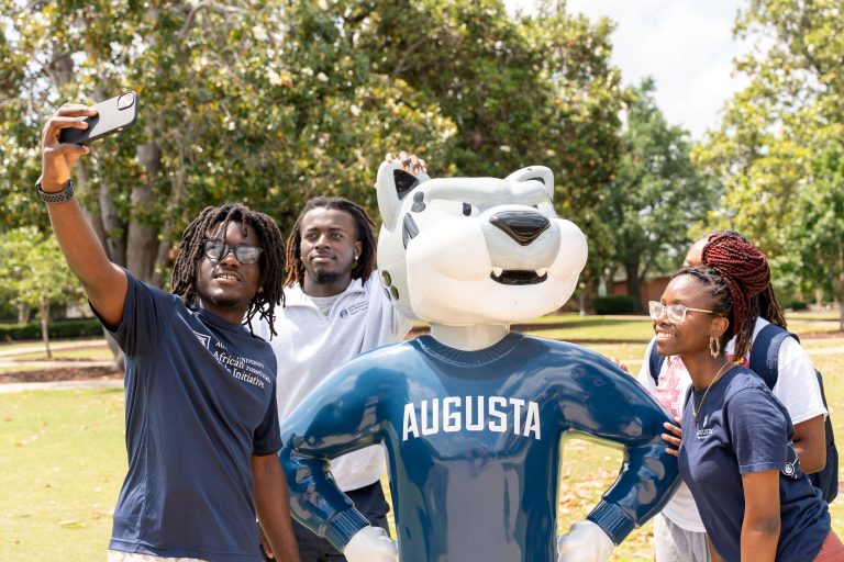 Four students surround the Augusta University mascot, Augustus, while taking a group picture.