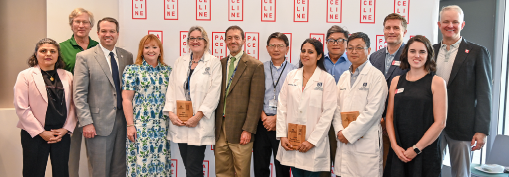 A group of researchers, university faculty and non-profit staff pose in front of a backdrop that reads "Paceline." The researchers hold awards in honors of grants they received.