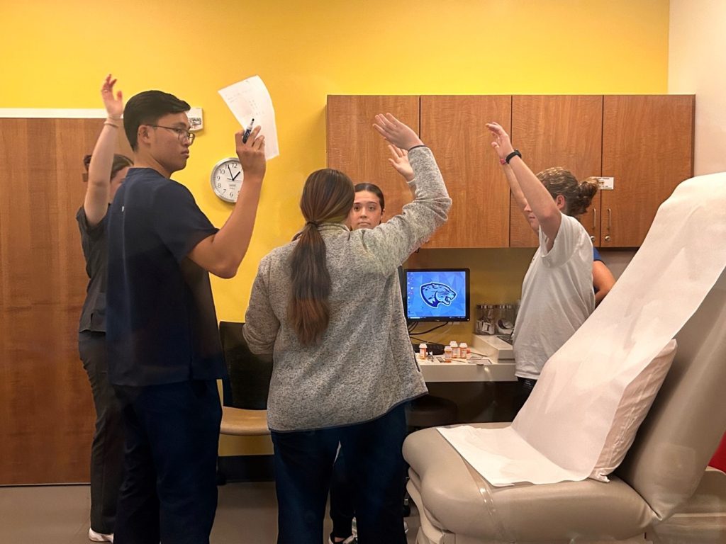 A group of five students stand in a circle with their hands raised.