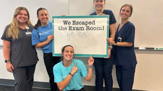 five females standing and kneeling around a sign that says "we escaped the escape room"
