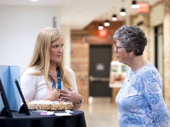 Two women talk in a hallway. One is explaining how her photo booth works while the other listens.
