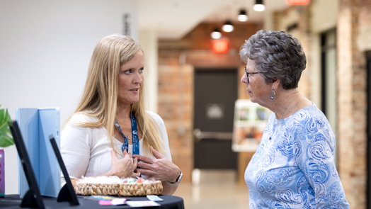Two women talk in a hallway. One is explaining how her photo booth works while the other listens.