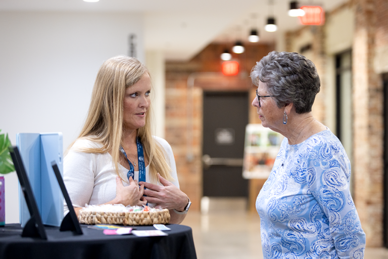Two women talk in a hallway. One is explaining how her photo booth works while the other listens.